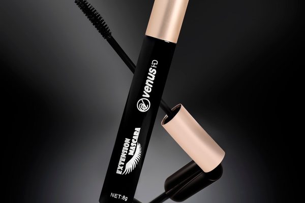 A sleek black mascara tube with a gold cap resting on a glossy black surface.