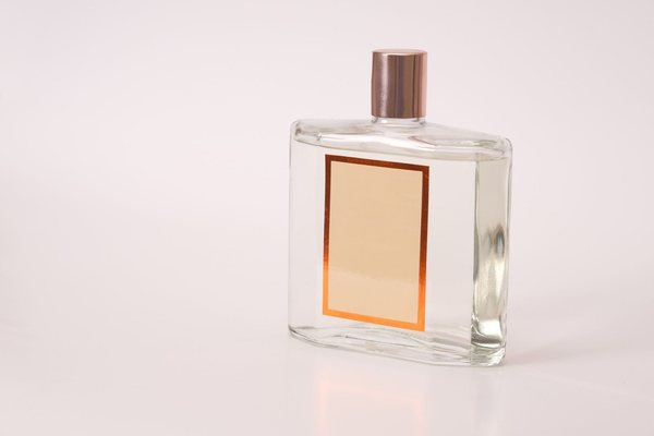 A clear glass perfume bottle with a blank label and a metallic cap standing on a plain light background.