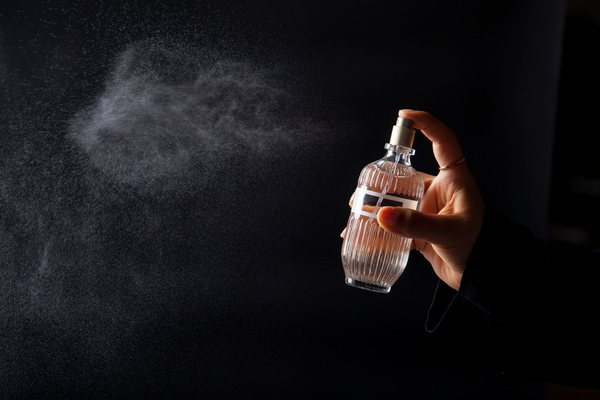 A hand spritzing a fine mist of perfume from a ribbed glass bottle against a dark background.